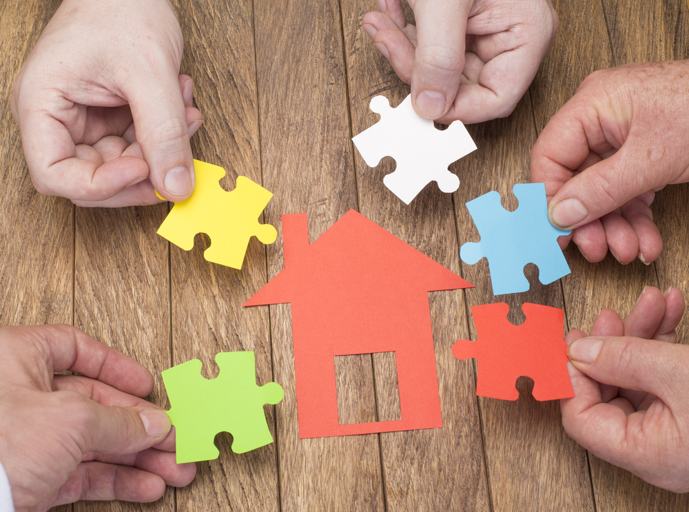 Multiple hands with jigsaw pieces representing a JBSP (Joint Borrower Sole Propreitor) home purchase with the help of family