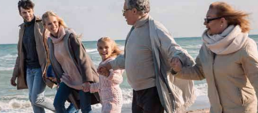 Happy generational family holding hands and smiling whilst walking along a beach